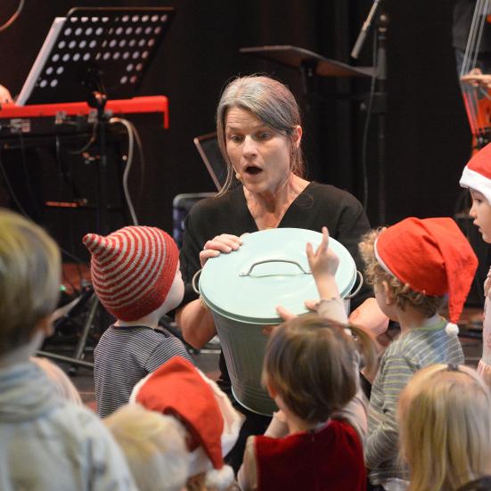 Billedet viser en gruppe børn med nissehuer foran en voksen kvinde med en skraldespand