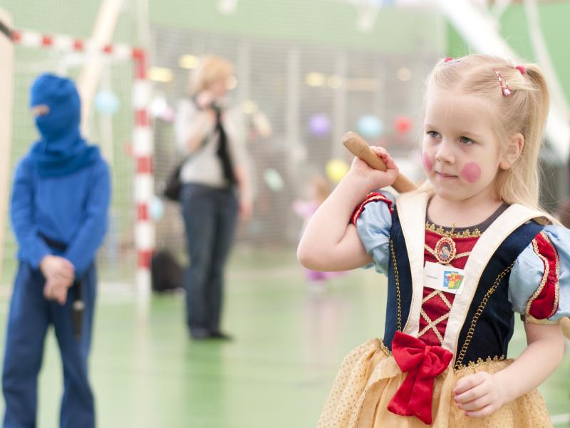 Billedet forestiller en pige til fastelavnsfest. Hun er klædt ud om en prinsesse og holder køllen klar til at slå katten af tønden.